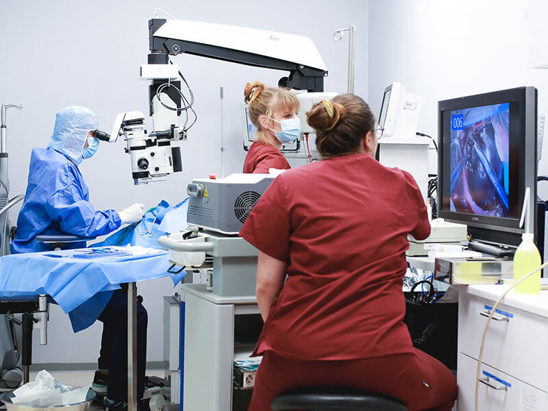 Équipe chirurgicale vétérinaire en tenue stérile réalisant une intervention avec microscope opératoire et écran de contrôle