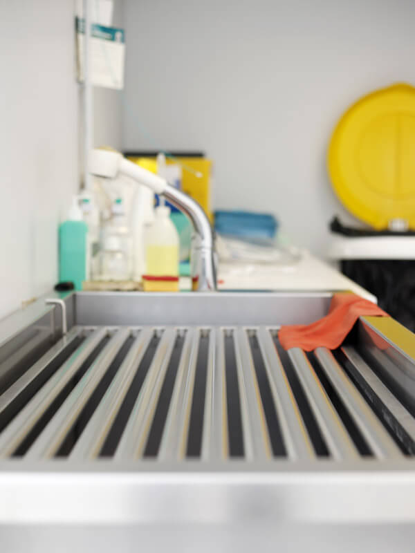 Évier médical en acier inoxydable avec grille d'évacuation striée et robinet professionnel dans la salle de soins